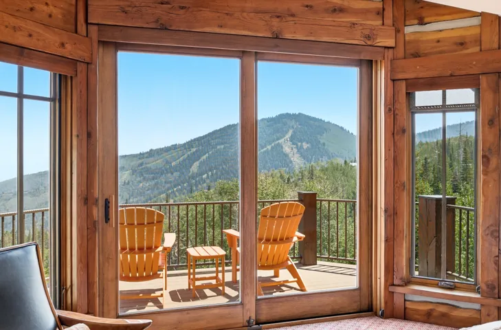 Wood-paneled interior walls, expansive sliding glass doors, multiple windows, and a private outdoor balcony with metal railing