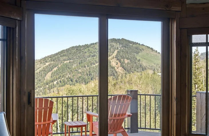 Sliding glass door opening to an outdoor deck with black metal railings, set against a backdrop of a distant tree-covered mountain