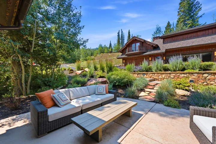 Expansive outdoor patio with natural stone retaining wall, stone slab steps, lush landscaping, and mature trees