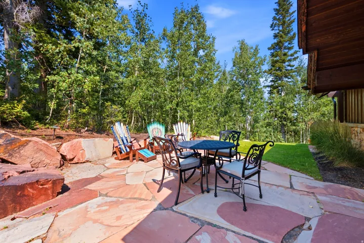 Expansive flagstone patio with natural stone retaining walls, surrounded by mature trees and a grassy area