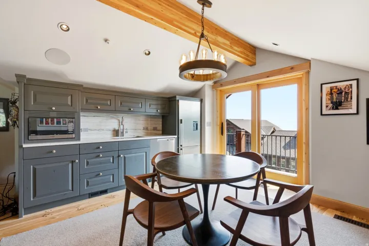 Custom cabinetry with integrated appliances, wood-finish flooring, exposed ceiling beam, recessed lighting, and balcony access