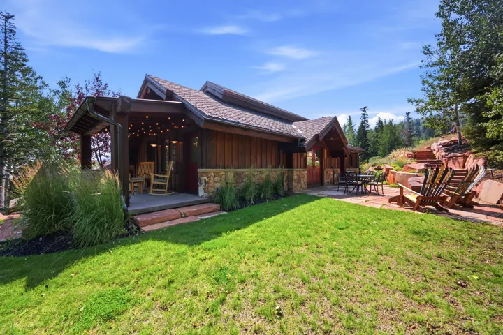 Wood siding exterior with stone accents, covered porch with built-in lighting, gabled roofline, and terraced hardscaping