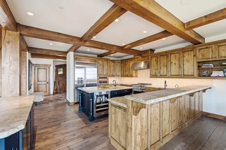 Kitchen featuring exposed wood ceiling beams, built-in stainless steel appliances, wood-finish flooring, stone countertops, and custom wood cabinetry