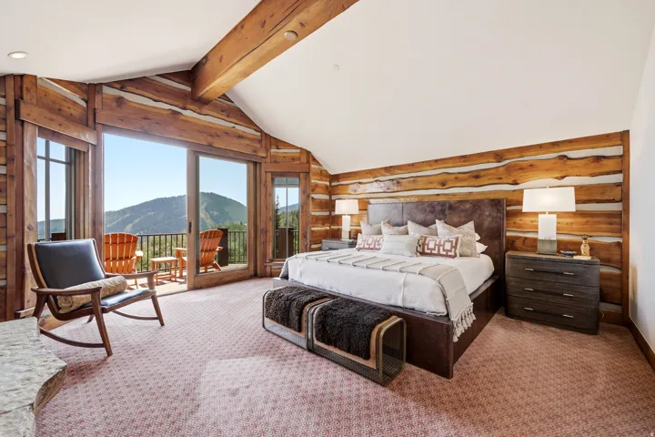 Vaulted ceiling with exposed wood beams, log-style interior walls, direct access to a private balcony, large sliding glass doors, and mountain scenery