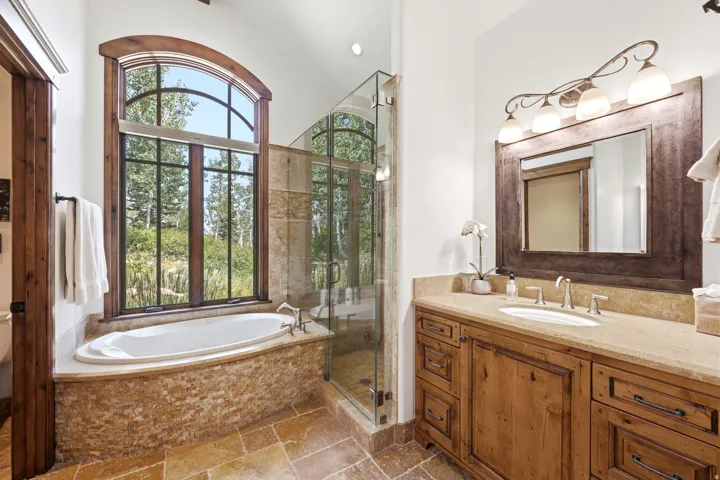 Soaking tub with stone surround, arched window, and glass-enclosed shower