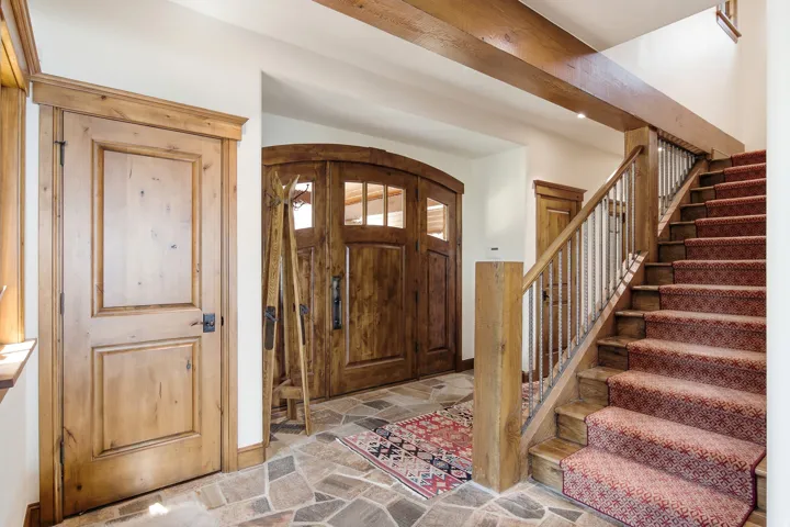 Flagstone flooring, arched wood entry door with glass panels, exposed wood beams, wood staircase with metal balusters, and wood interior doors