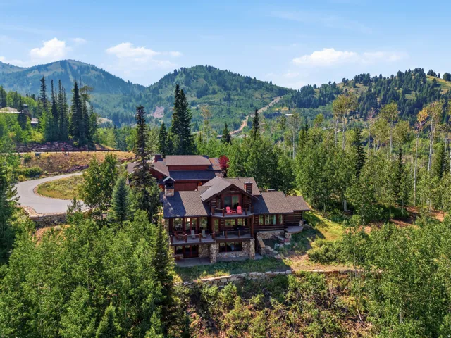 Log home exterior with multiple balconies, stone foundation, and a shingle roof, surrounded by mature trees