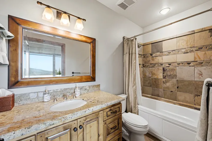 Vanity with stone countertop, natural wood finish cabinetry, rectangular undermount sink, and a framed mirror