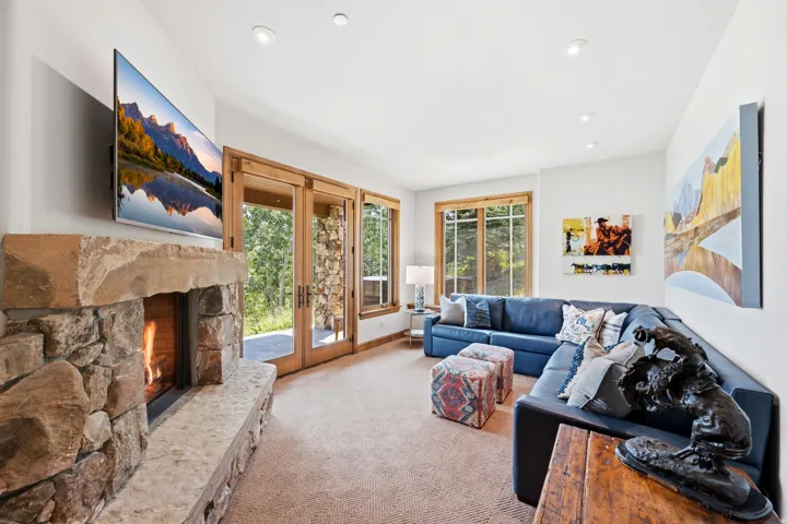 Stone-clad fireplace, built-in television, light wood-finish French doors, recessed lighting, and carpeted flooring