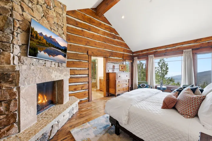 Stone-clad fireplace, log-style wall construction, vaulted ceiling, wood-finish flooring, and expansive windows