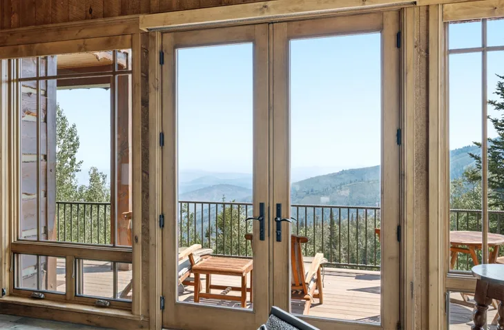 Wooden french doors opening to a deck, featuring panoramic mountain scenery, natural wood-finish walls, and expansive windows