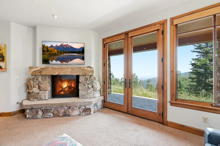 Corner stone fireplace with a stone mantel, wood-framed glass doors, and large picture windows