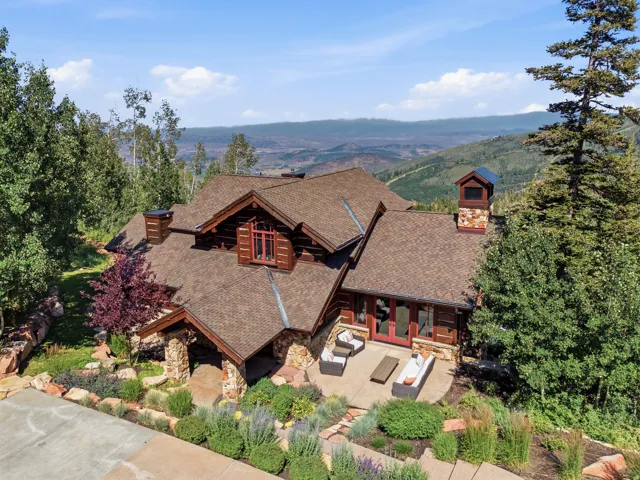Architectural shingles, log and stone exterior, multiple chimneys, landscaped grounds with diverse plantings, and a stone patio