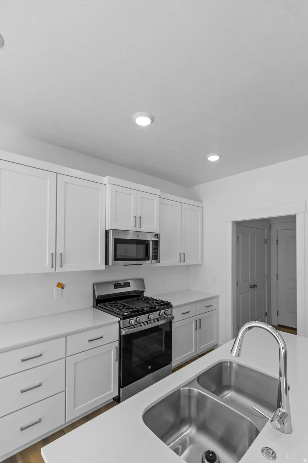 White shaker cabinetry, stainless steel appliances, integrated double basin sink, white countertops, and recessed lighting