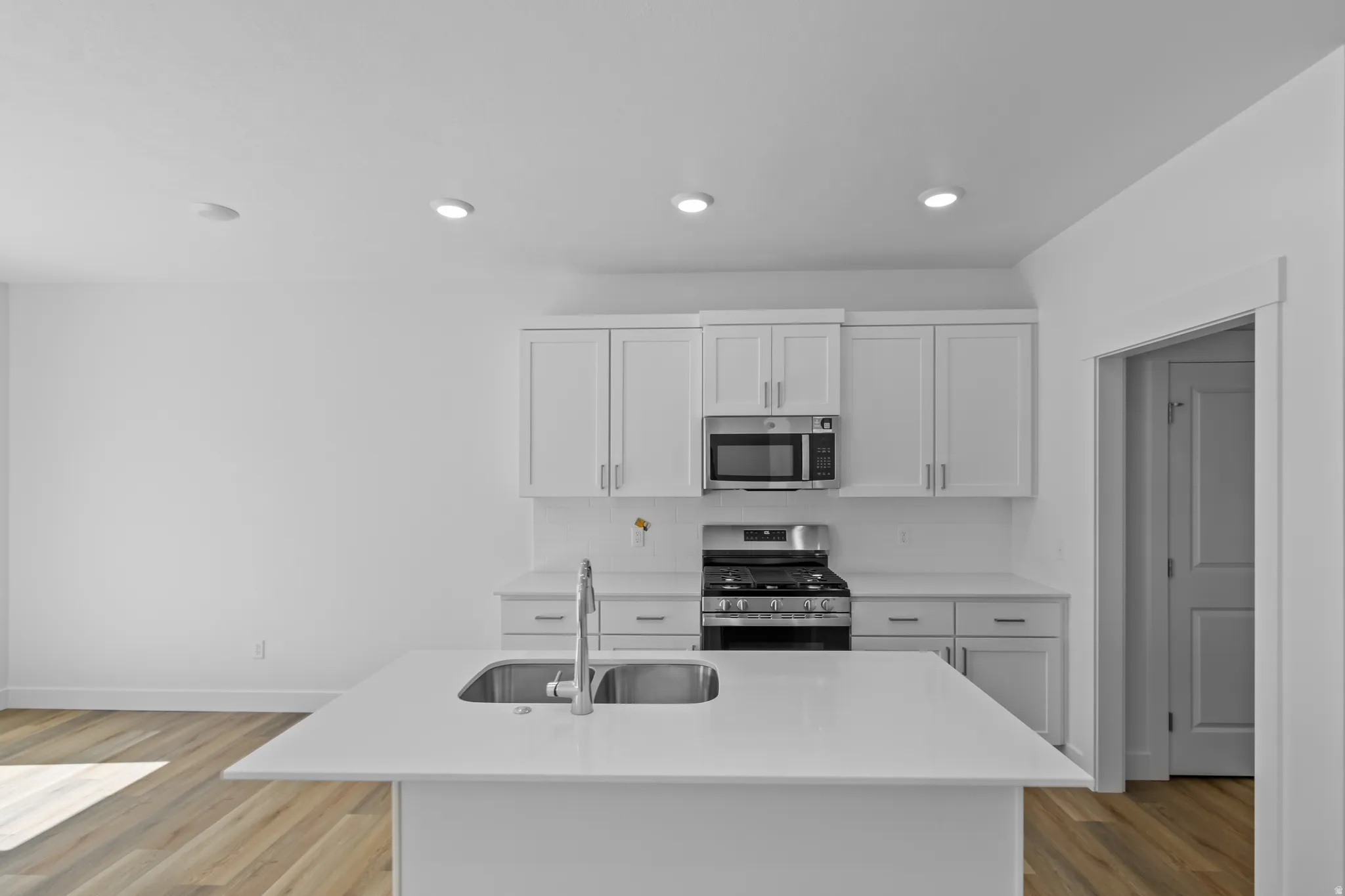 White cabinetry with stainless steel appliances, a center island with an undermount double basin sink, and wood-finish flooring