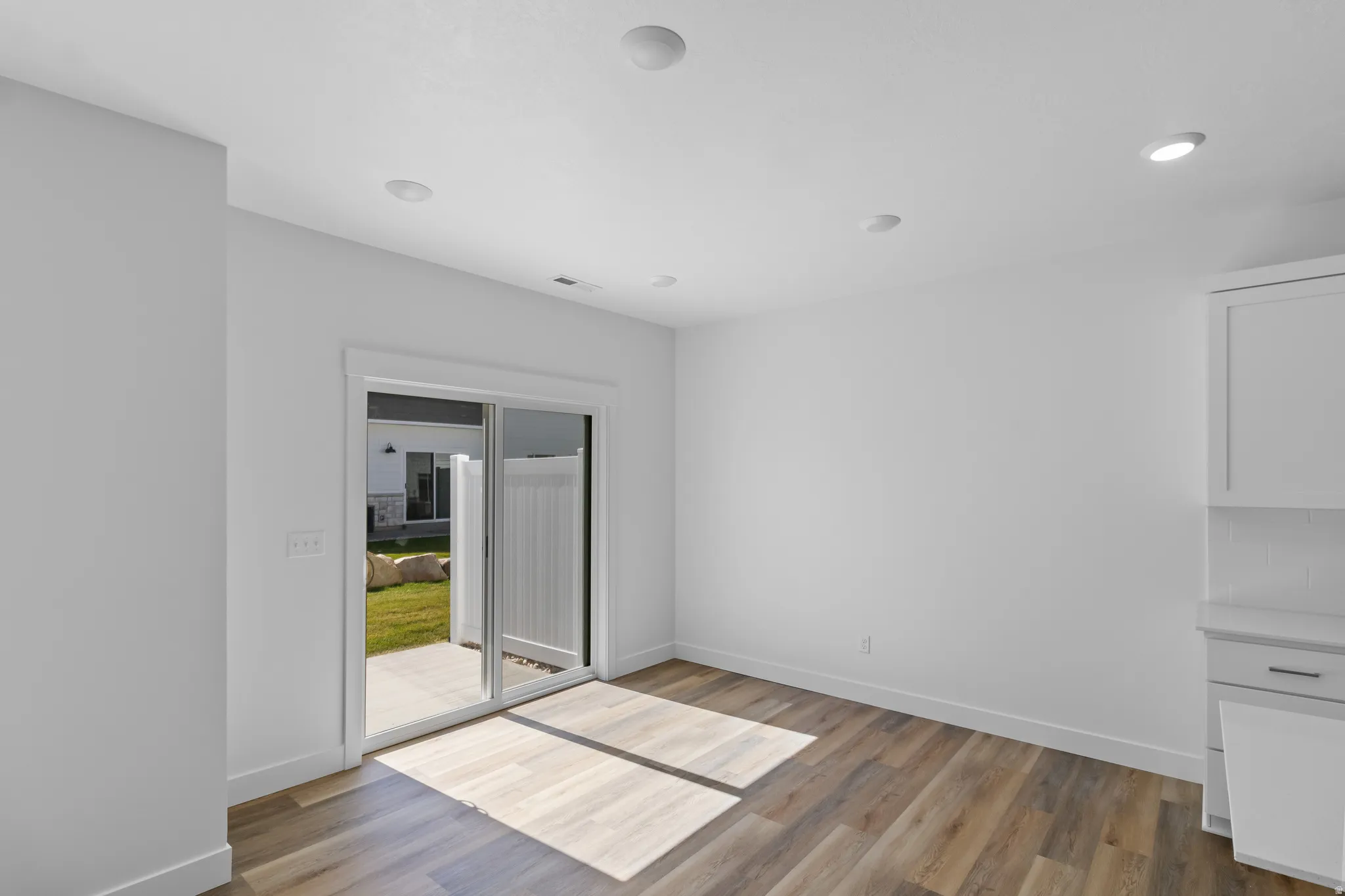 Wood-finish flooring, recessed lighting, sliding glass door, white cabinetry, and a private patio