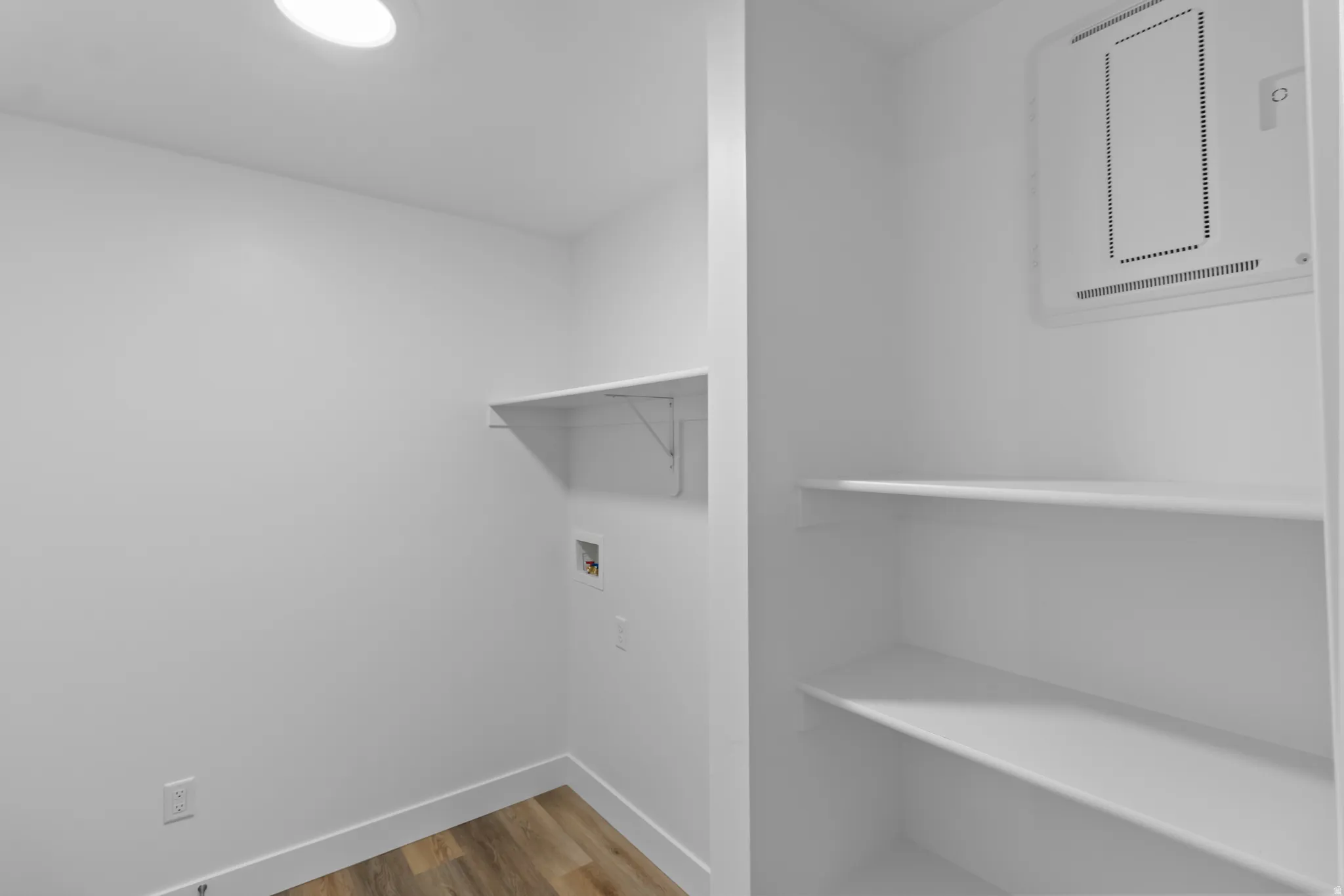 Laundry area featuring wood-finish flooring, overhead lighting, and built-in shelving