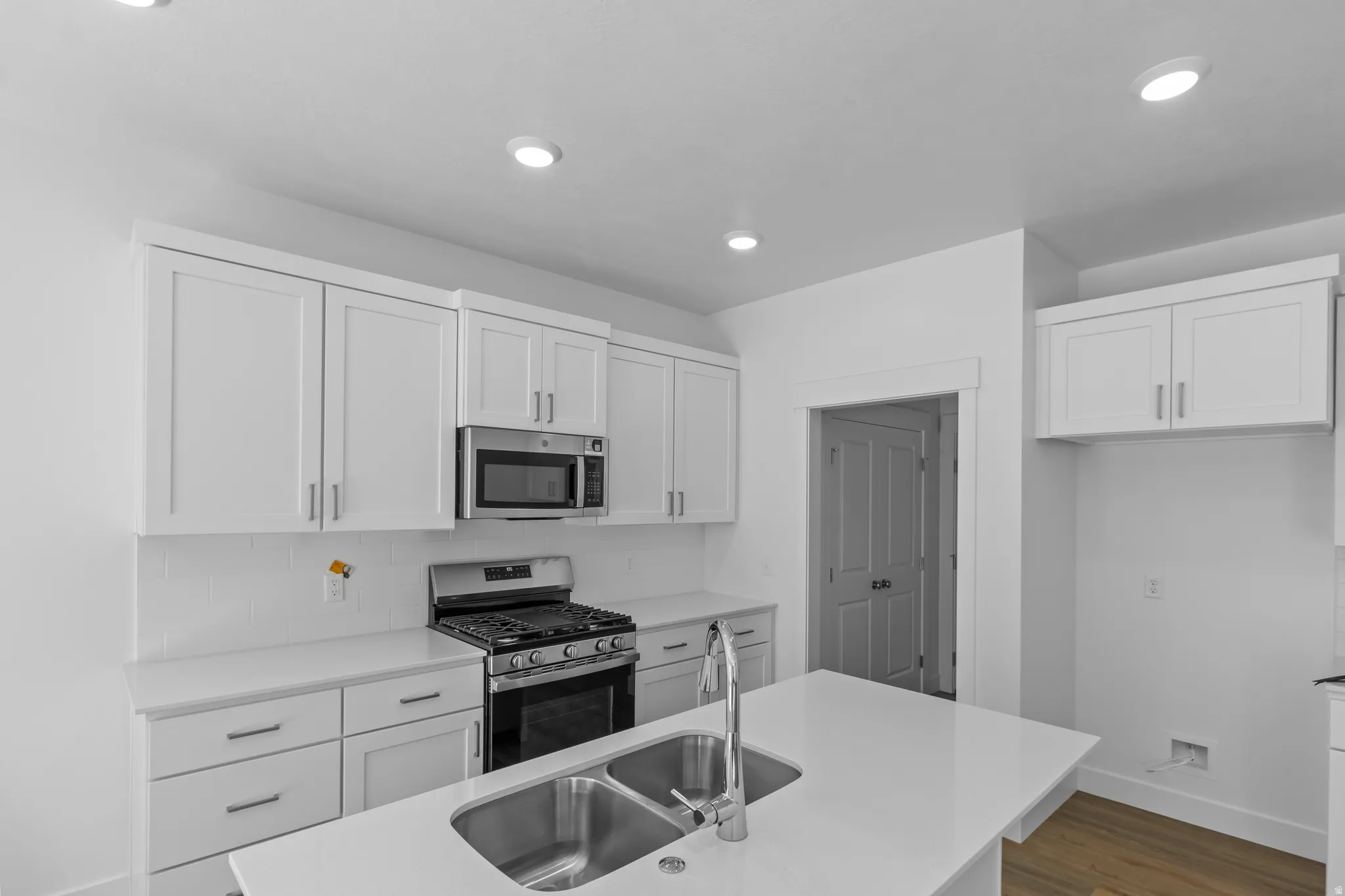 Modern kitchen with white shaker cabinetry, stainless steel appliances, a center island featuring a double-basin sink, and recessed lighting