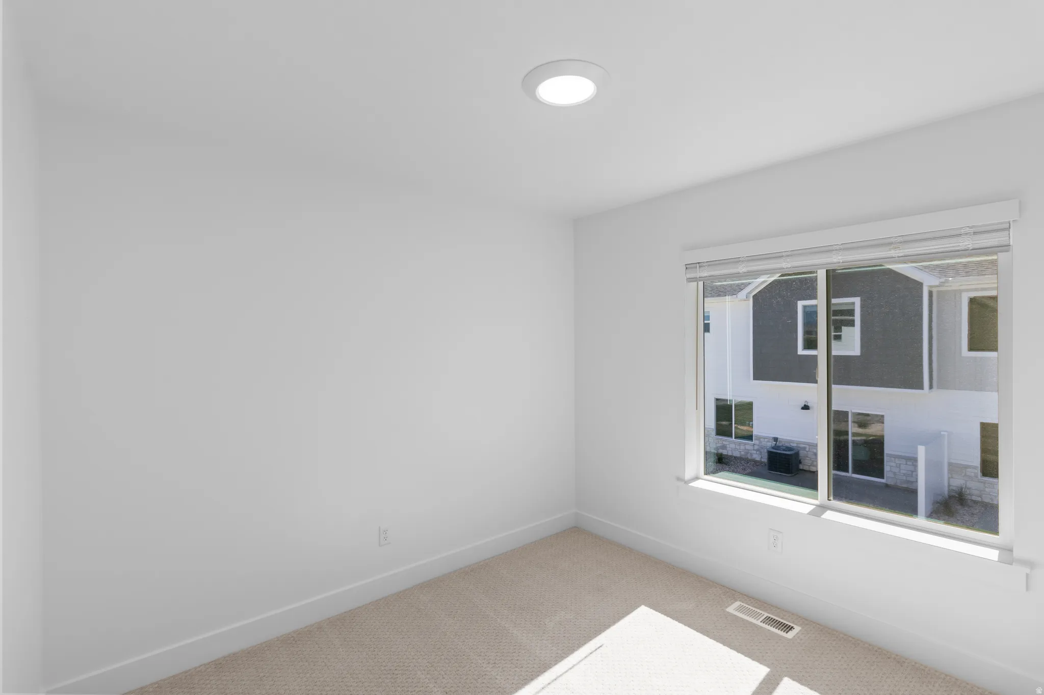 Recessed ceiling light fixture, white walls, carpeted flooring, large window with blinds, and white trim