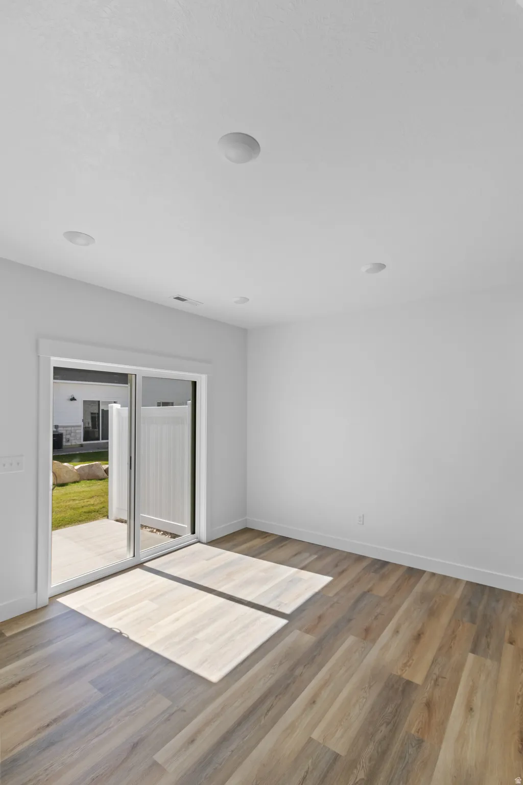 Wood-finish flooring throughout, white painted walls, recessed lighting, and sliding glass patio doors opening to a hardscaped patio