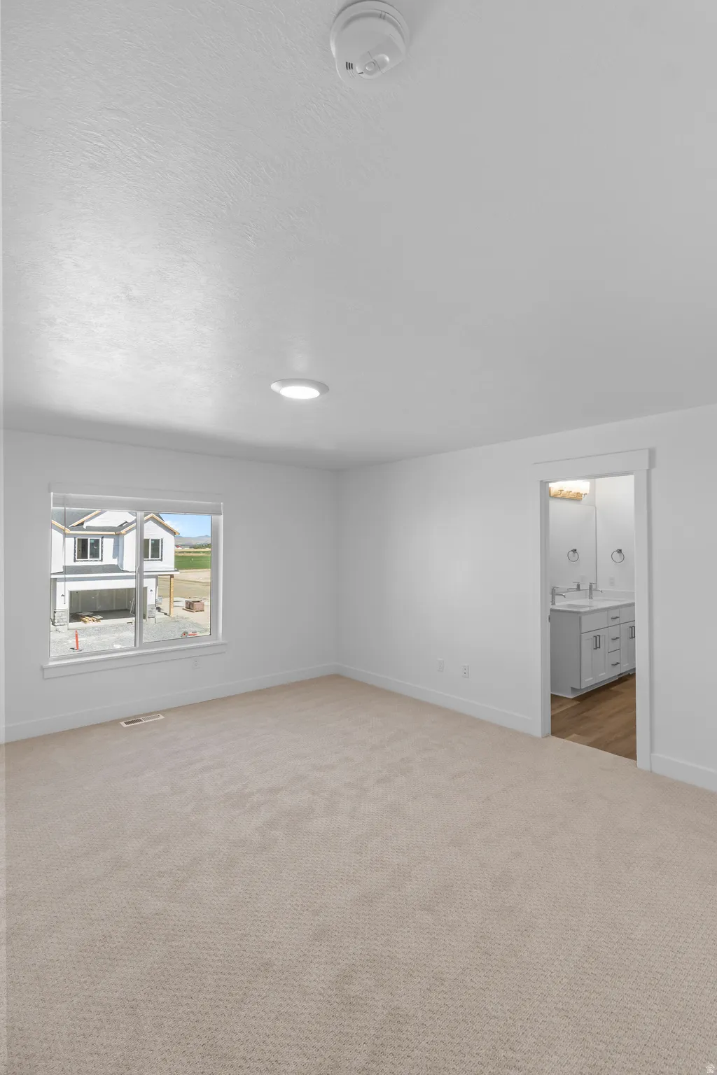 Plush carpet flooring, recessed ceiling lighting, white window trim, and a doorway opening to a bathroom with dual vanities