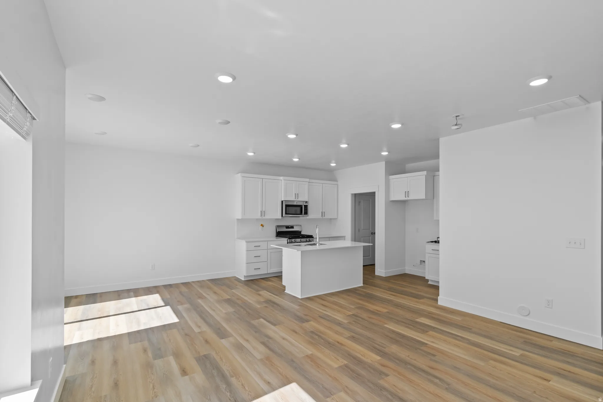 Recessed lighting throughout, wood-finish flooring, white cabinetry, a kitchen island, and stainless steel appliances