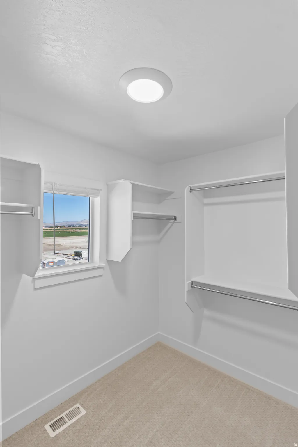 Built-in closet shelving and hanging rods, ceiling-mounted light fixture, and window with natural light