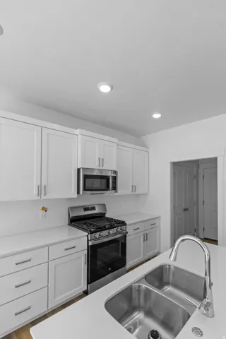 White shaker cabinetry, stainless steel appliances, integrated double basin sink, white countertops, and recessed lighting