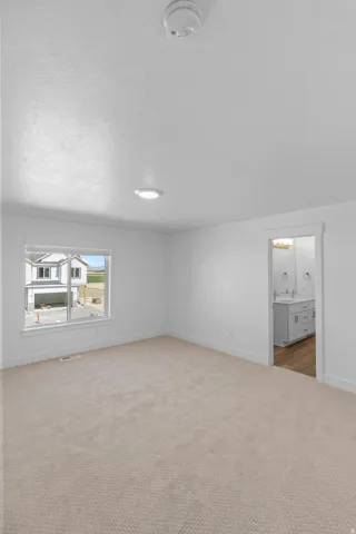 Plush carpet flooring, recessed ceiling lighting, white window trim, and a doorway opening to a bathroom with dual vanities