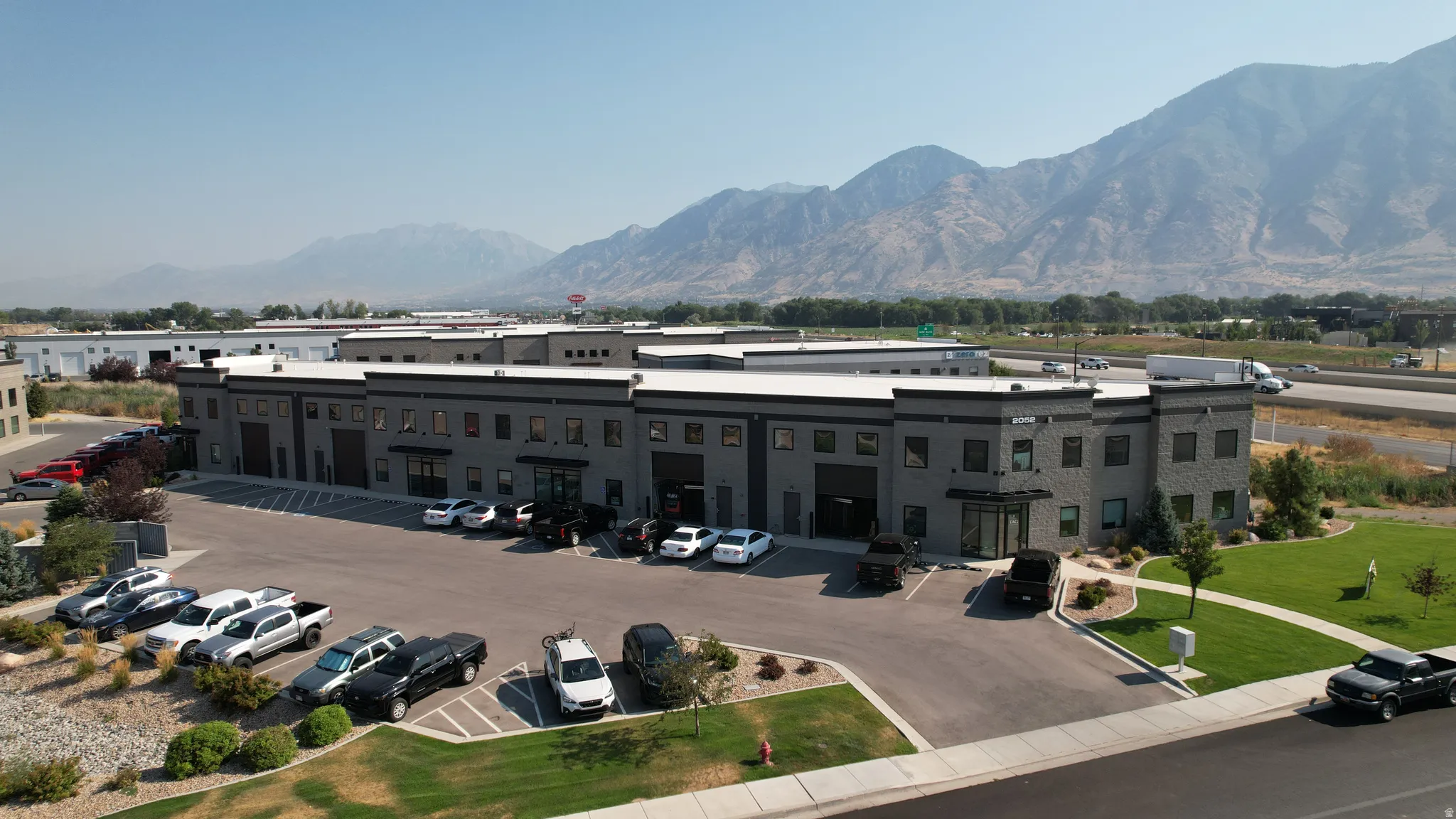 Modern commercial building with dark gray exterior, multiple large bay doors, extensive paved parking, and manicured landscaping