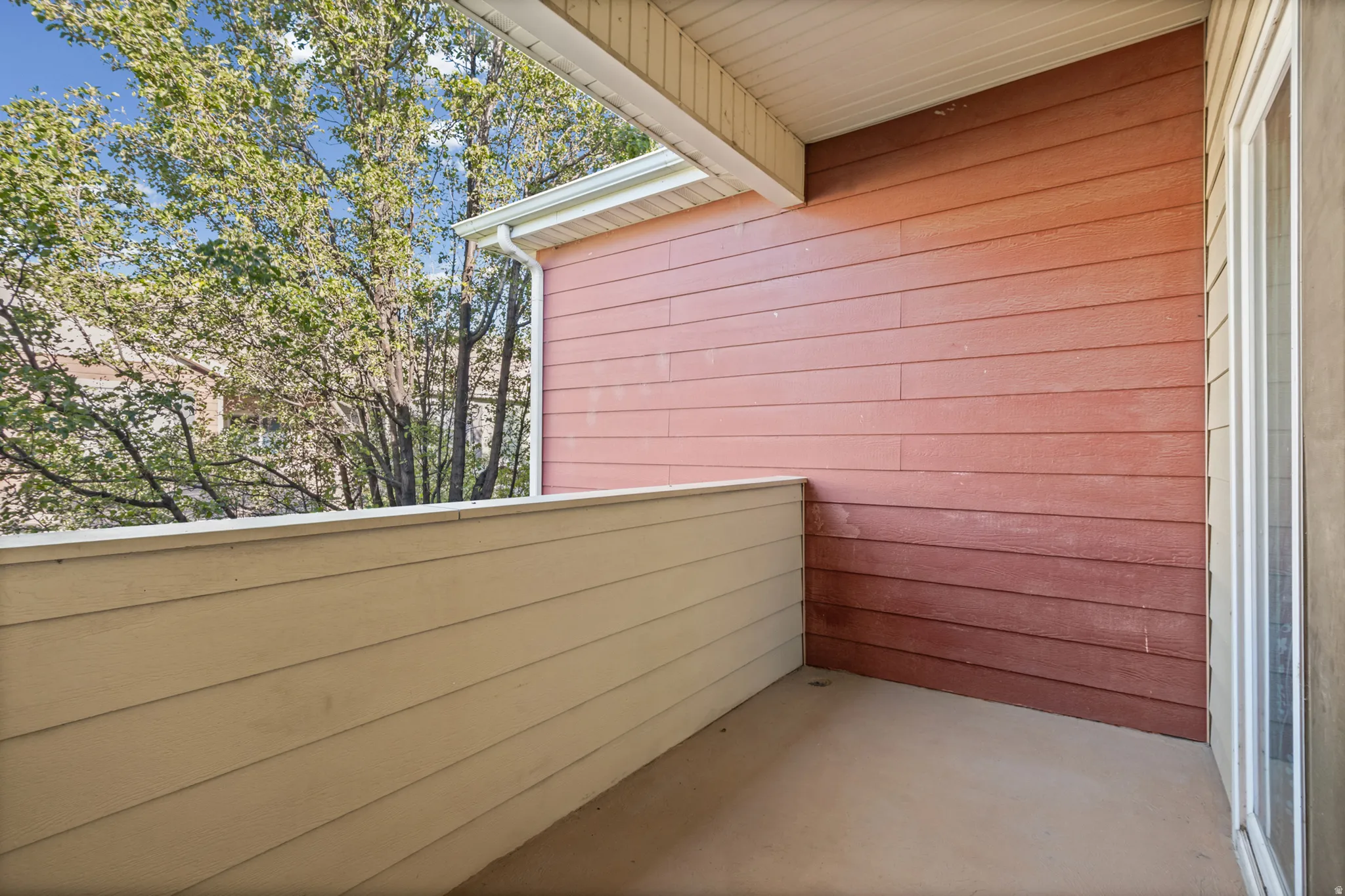 Outdoor patio featuring composite decking, wood-look siding, a white gutter system, and a sliding glass door