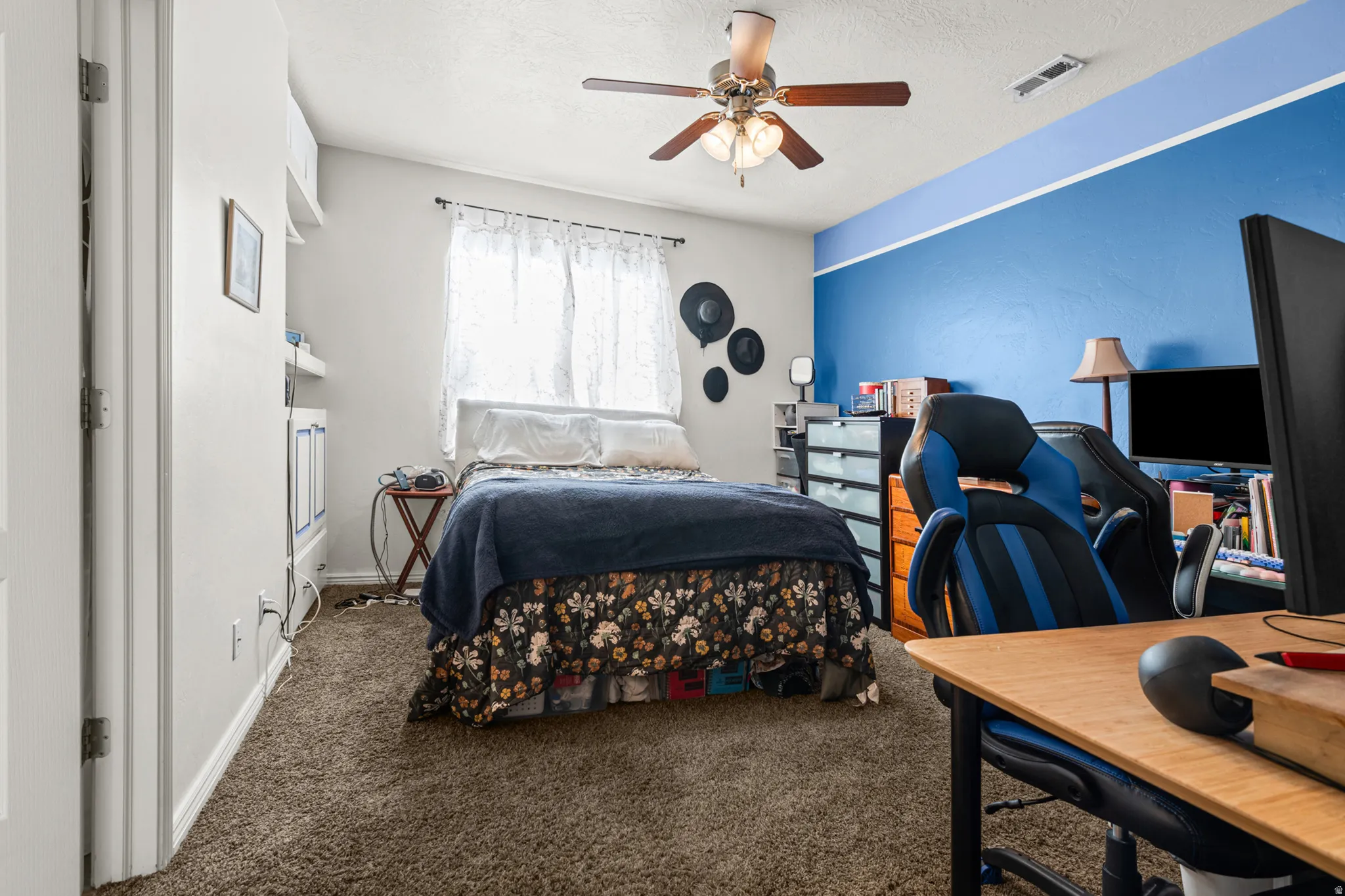 Carpeted interior room featuring a ceiling fan with light fixture, window with drapes, and a partially visible built-in shelving unit