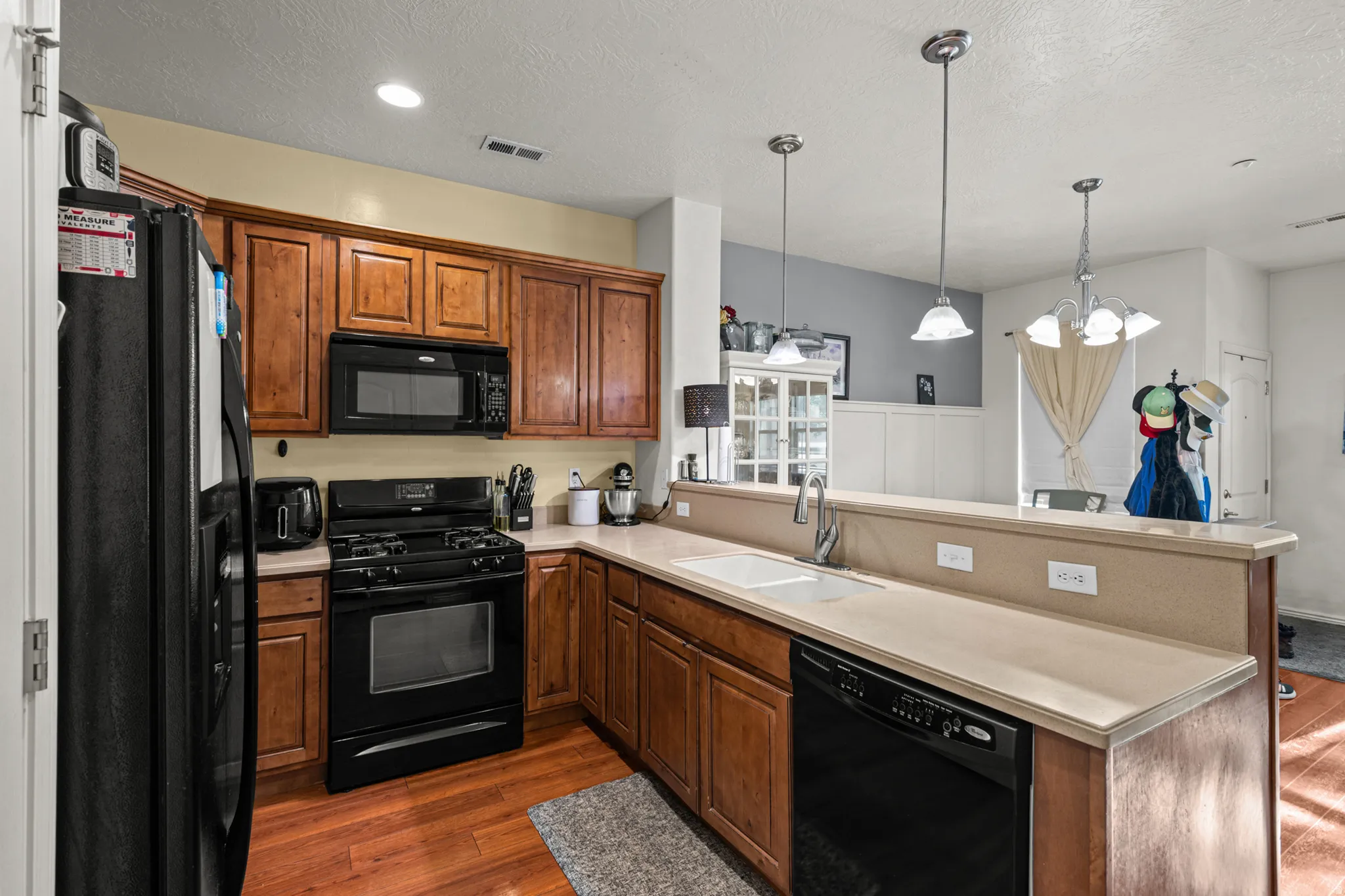 Kitchen featuring wood-finish flooring, warm-toned cabinetry, and black appliances