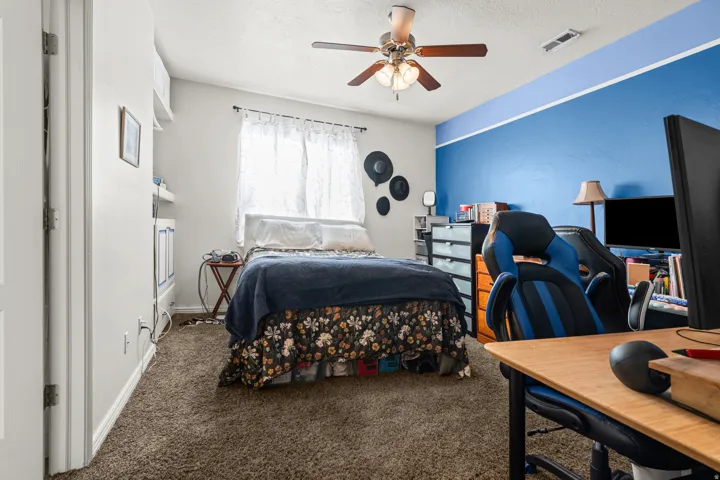 Carpeted interior room featuring a ceiling fan with light fixture, window with drapes, and a partially visible built-in shelving unit