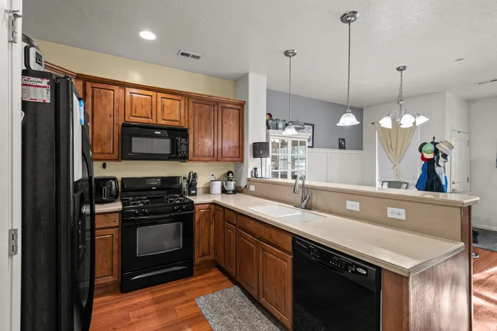 Kitchen featuring wood-finish flooring, warm-toned cabinetry, and black appliances