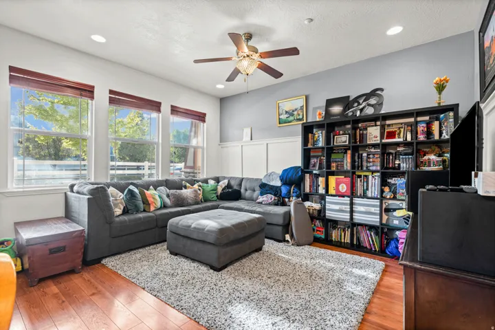 Living area featuring wood-finish flooring, recessed lighting, a ceiling fan with integrated lighting, and three large windows with window treatments