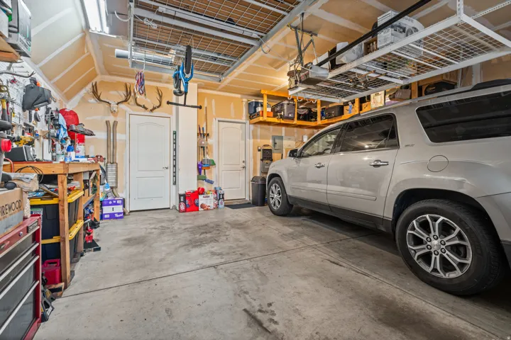 Attached garage featuring concrete flooring, overhead storage racks, a workbench, and two interior access doors