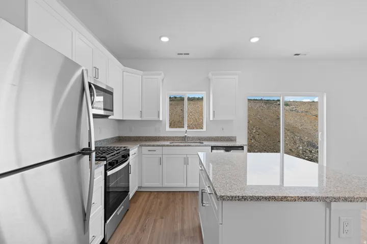 Kitchen featuring white cabinetry, stainless steel appliances, speckled countertops, wood-finish flooring, and a central island