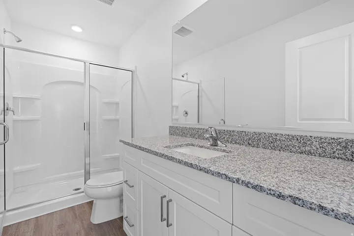 Walk-in shower with sliding glass doors, white vanity with shaker-style cabinetry, chrome hardware, granite-style countertop, and wood-finish flooring