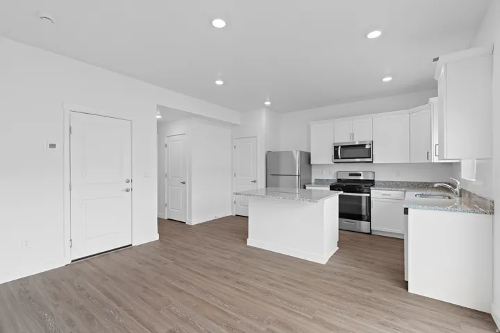 Open-concept kitchen with wood-finish flooring, white cabinetry, granite countertops, and stainless steel appliances