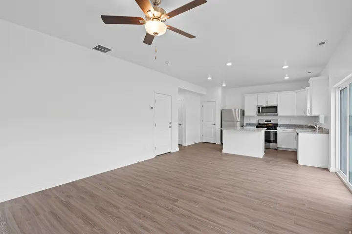 Open-concept living space featuring wood-finish flooring, a contemporary ceiling fan, recessed lighting, and a kitchen with white cabinetry and stainless steel appliances