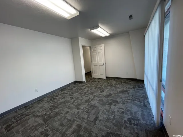 Spacious room featuring gray patterned carpet, white walls, and a large window with vertical blinds