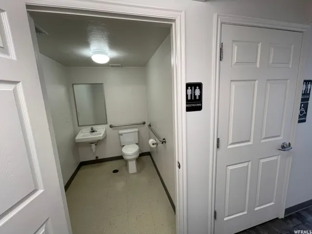 Restroom featuring a wall-mounted sink, toilet, grab bars, and a wall mirror