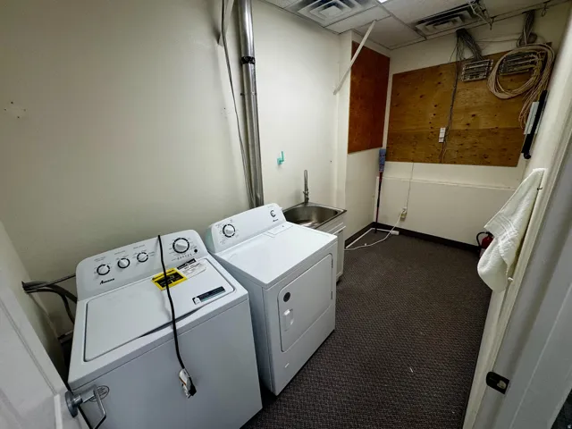 Utility area featuring a stainless steel sink, dark carpet flooring, and white walls