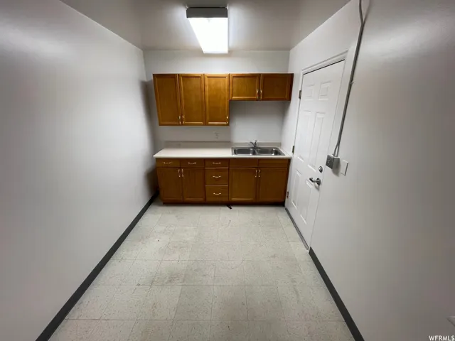 Utility space featuring wood-finish cabinetry, a double basin stainless steel sink, and light-toned countertops