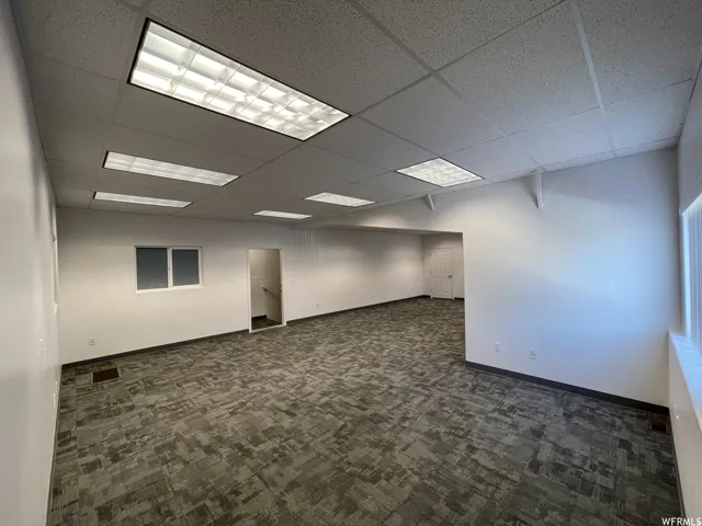Spacious interior featuring neutral carpeting with a textured pattern, drop ceiling with recessed lighting, and white painted walls