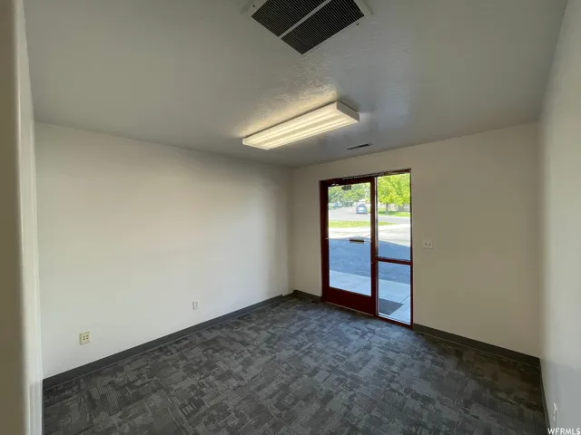 Commercial space featuring neutral-toned walls, patterned carpet flooring, and a glass-paneled entry door