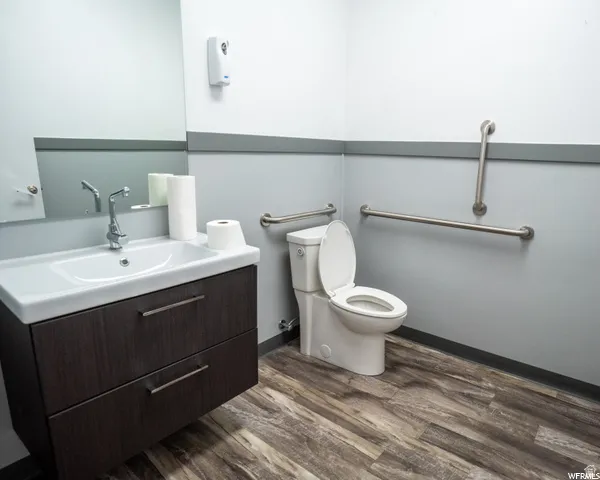 Floating vanity with integrated basin, chrome faucet, wood-finish flooring, and wall-mounted grab bars