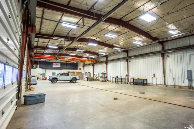 High-bay industrial space featuring a concrete floor, exposed steel beam construction, overhead lighting, and a large roll-up door