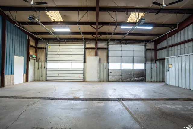 Concrete flooring, two overhead doors with windows, exposed ceiling beams, and fluorescent lighting